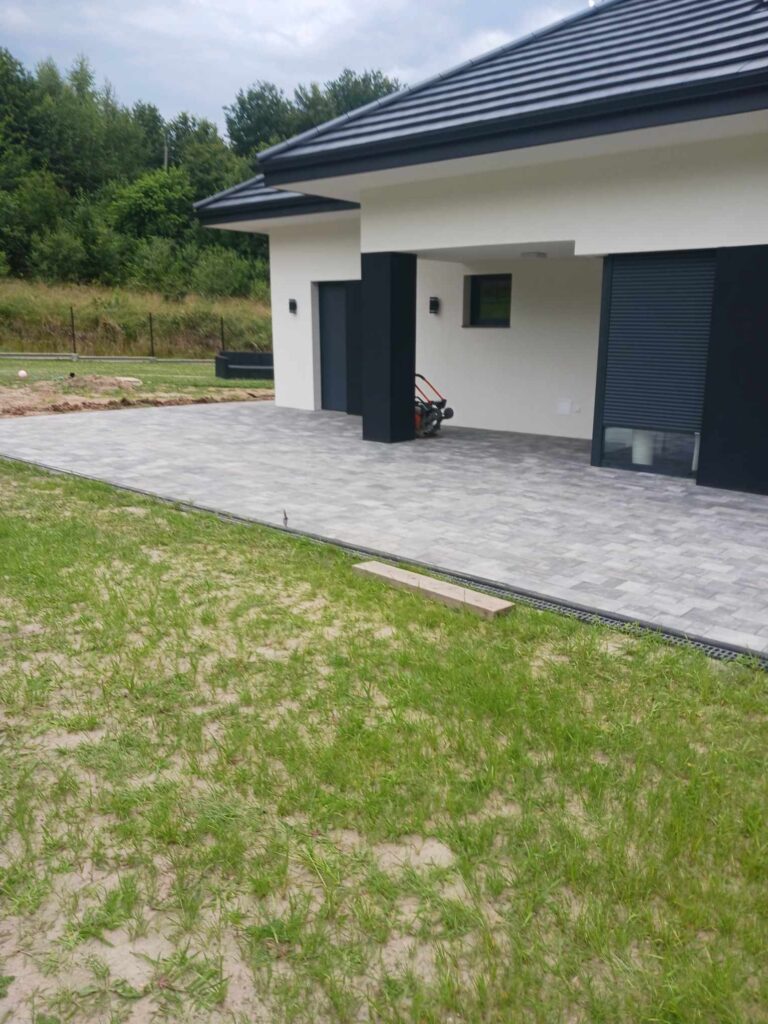 Taras pod domem z kostku brukowej zrównany z poziomem ogrodu
