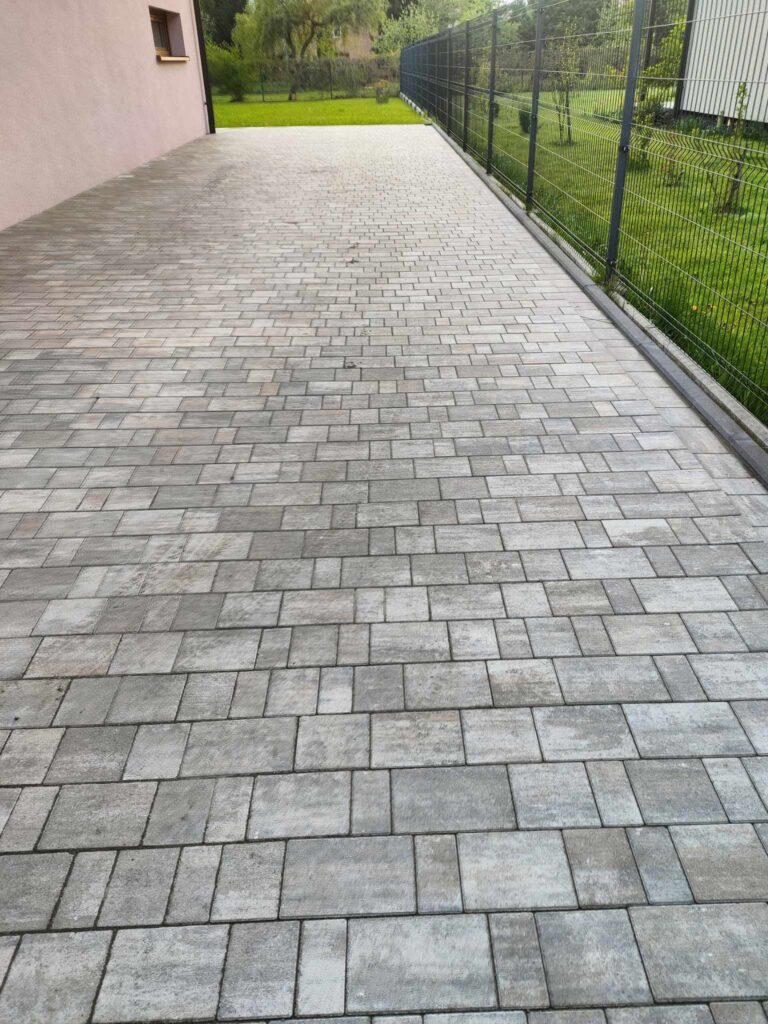 a brick walkway with a fence and grass